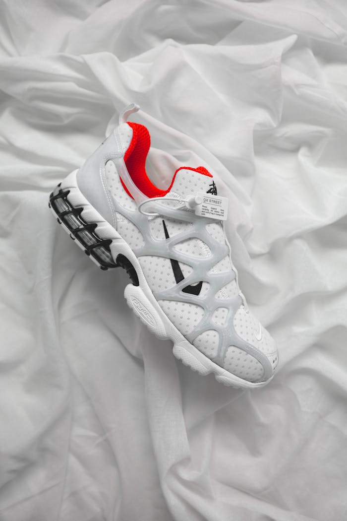 home-hero Stylish white athletic sneaker with red accents on a textured white fabric background.